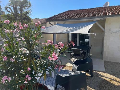 une terrasse avec une table, des chaises et des fleurs roses dans l'établissement Calme et ensoleillée Maison au pied de la plage entre St Palais sur Mer et Royan, à Vaux-sur-Mer