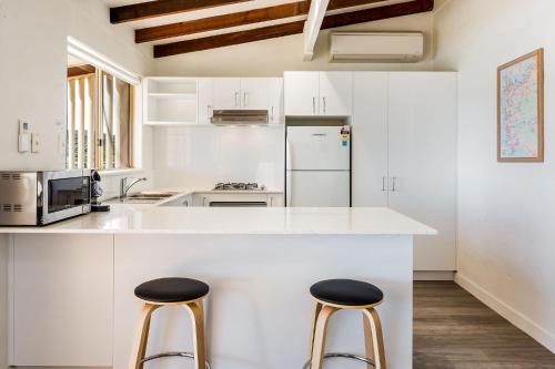 a white kitchen with two stools at a counter at Canal Rocks Beachfront Apartments in Yallingup