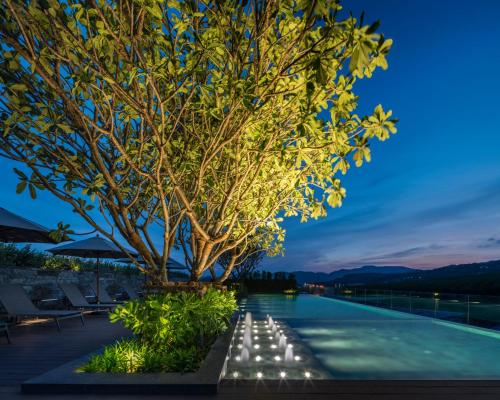 a tree on the edge of a swimming pool at night at Ramada Plaza by Wyndham Chao Fah Phuket in Phuket Town