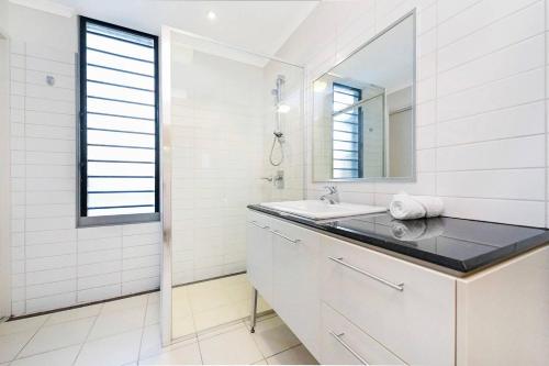 a white bathroom with a sink and a mirror at Artistic City Escape with Balcony and Parking in Darwin
