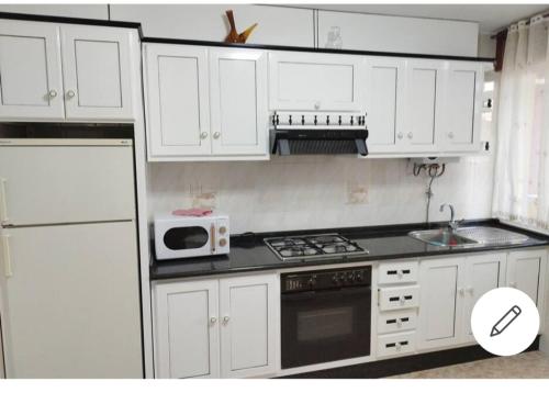 uma cozinha com armários brancos, um fogão e um micro-ondas em Vivienda 2 sin ascensor em Laxe