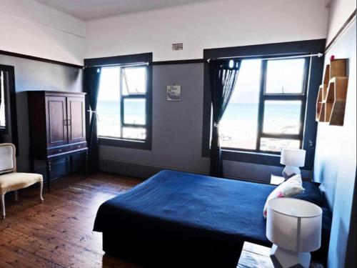 a bedroom with a blue bed and two windows at African Soul Surfer in Muizenberg
