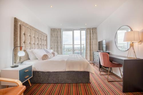 a bedroom with a large bed with a desk and a computer at Austin David Apartments ExCeL in London