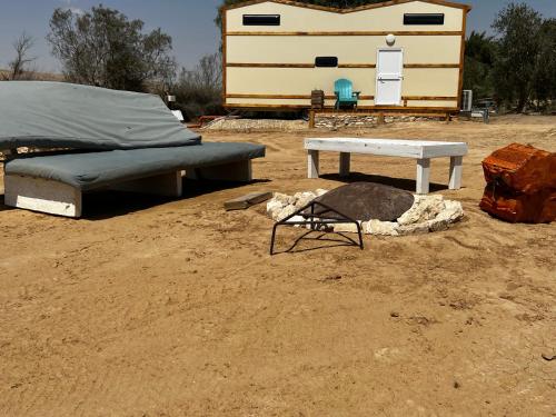 a bed and a table in the dirt with a trailer at צימראוון בחוות זית המדבר in Sede Boqer