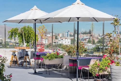 two white umbrellas on a patio with tables and plants at Palla Boutique Hotel in Arequipa