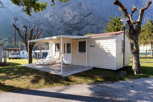 ein kleiner weißer Schuppen mit einem Baum und Bergen im Hintergrund in der Unterkunft Camping Daino in Pietramurata