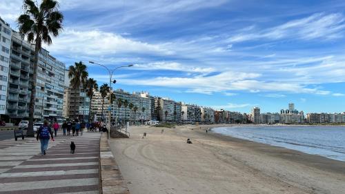 einen Strand mit Gebäuden und Menschen, die darauf laufen in der Unterkunft Frente a la Playa Pocitos! in Montevideo