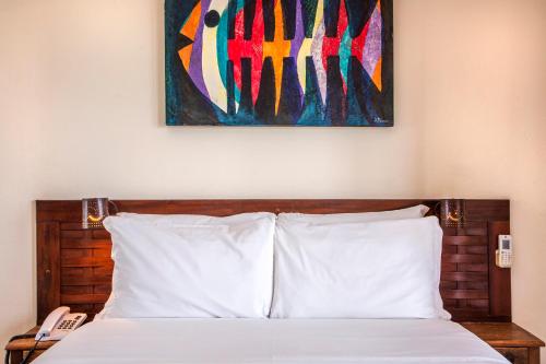 a bedroom with a bed with a painting above it at Barra do Piuva Porto Hotel in Ilhabela