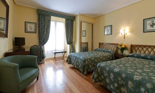 a hotel room with two beds and a chair at Hotel Norte y Londres in Burgos