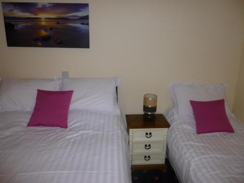 two beds in a bedroom with purple pillows and a night stand at The Schooner Tavern in Ballycotton