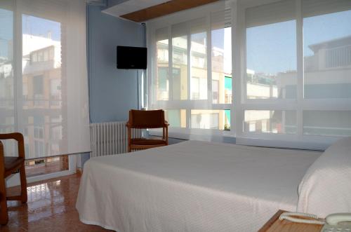 a bedroom with a white bed and a large window at Hotel Cervantes in Alicante