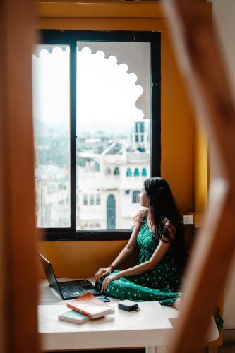 a woman in a green dress sitting in a window with a laptop at Citylights By MUSAFIR in Udaipur