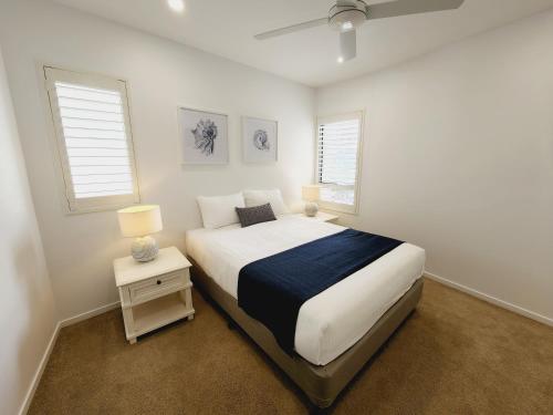 a white bedroom with a bed and two windows at The Dunes Cotton Tree in Maroochydore