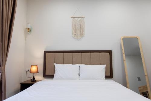 a bedroom with a white bed with a mirror and a lamp at Dalat Blanc Hotel & Apartment in Da Thanh