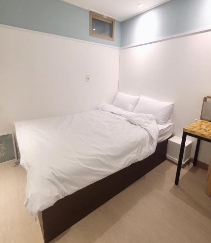 a bed with white sheets and pillows in a room at Well Plus Guest House in Seoul