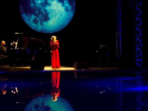 a woman standing on a stage in front of a moon at Thalatta Seaside Hotel in Ayia anna