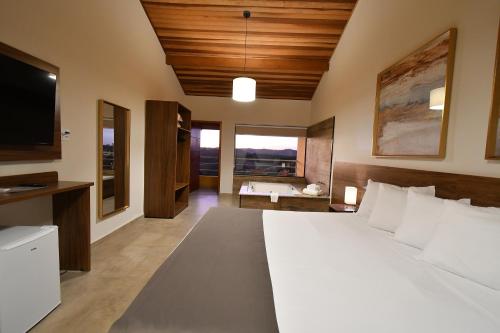 Un dormitorio con una gran cama blanca y un televisor. en Molise Hotel Fazenda, en Serra Negra