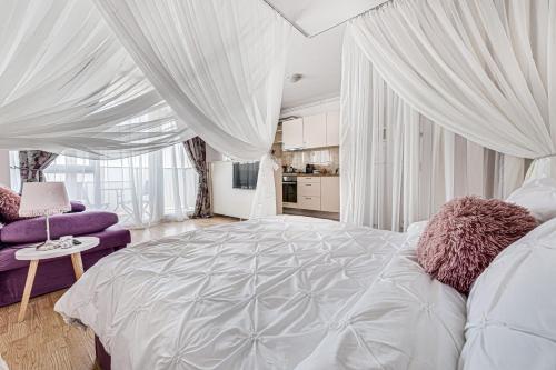a white bedroom with a large bed and a purple couch at ARI Purple Studio in Arad