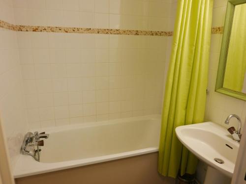La salle de bains est pourvue d'une baignoire, d'un lavabo et d'un rideau de douche jaune. dans l'établissement Studio cabine 4 pers, balcon, proche pistes et centre, garage sous-sol, tout équipé - FR-1-263-436, à Valloire