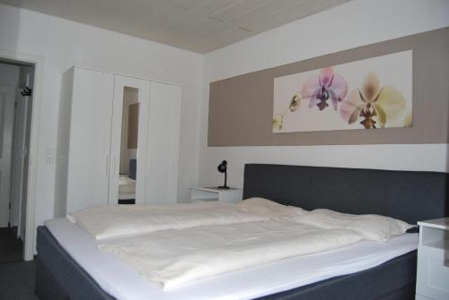 1 dormitorio con 1 cama con sábanas blancas y flores en la pared en Ferienwohnung-Stricker-2-1-Typ-B-Terrasse, en Walkenried