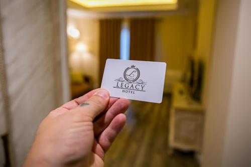a person holding up a card with a legacy hotel sign at Legacy Boutique Hotel in Korçë