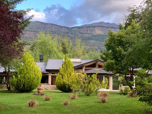 une maison avec un jardin arboré et des montagnes en arrière-plan dans l'établissement CABAÑAS AILIN-CO, à El Bolsón