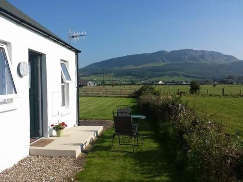 a patio with a table and chairs next to a white house at Ballymultimber Cottages in Limavady