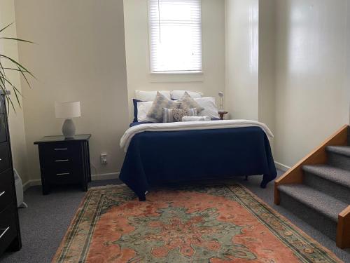 a bedroom with a bed with a blue bedspread and a rug at Private, comfortable studio. in Wellington