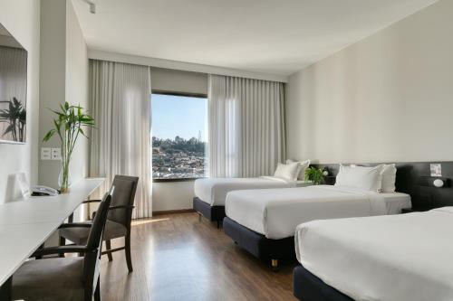 a hotel room with two beds and a desk at Mercure Belo Horizonte Lourdes in Belo Horizonte