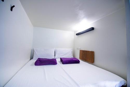 a small bedroom with a white bed with purple pillows at 黑背包 Black Backpack in Xiaoliuqiu