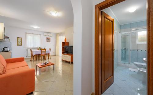 salon z pomarańczową kanapą i łazienką w obiekcie Family friendly apartments with a swimming pool Basanija, Umag - 3402 w mieście Savudrija