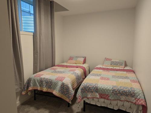 two twin beds in a room with a window at Livingston Howse Haven - A simple & cozy private two-bedroom basement suite with free parking in Calgary
