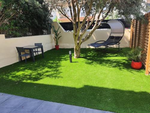 a green yard with a table and a tree at Superbe appartement avec jacuzzi et extérieur in Perpignan