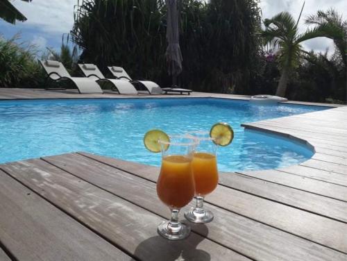 two glasses of orange juice sitting on a table near a swimming pool at Villa Kajou in Sainte-Anne