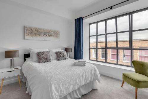a white bedroom with a bed and a chair and windows at Norwich Castle View Apt - Modern 2 Br in Norwich