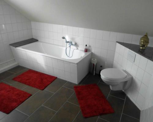 y baño con bañera, aseo y alfombras rojas. en Haus Abel, en Aerzen