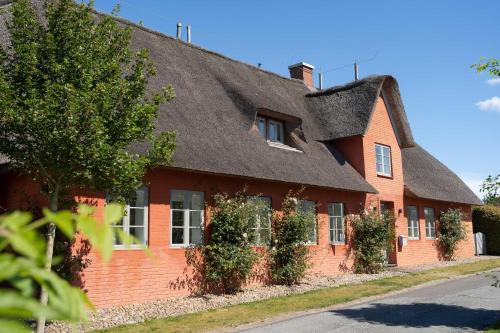 a red brick house with a thatched roof at Reethus Doerpsend Haus 2 in Midlum