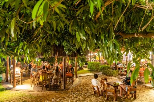 a group of people sitting in chairs under a tree at La Cozinha Bungalow in Barra Grande