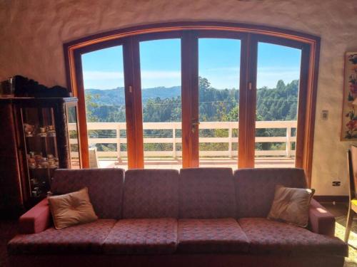 a couch in a living room with a large window at Alto do Capivari - Gramado e vista espetacular in Campos do Jordão
