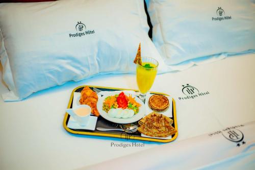 a tray of food and a drink on a bed at Prodiges Hôtel in Yaoundé