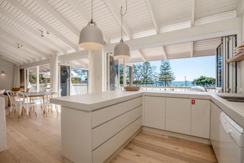 a kitchen with white cabinets and a dining room with a table at Barbara by Kinsfolk in Byron Bay