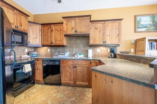 a kitchen with wooden cabinets and black appliances at Bear's Paw Chalet - Amazing Location & Ski In-Out in Big White