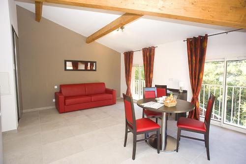a living room with a table and a red couch at The Originals City, Hôtel Les Bastides du Gapeau in Solliès-Toucas