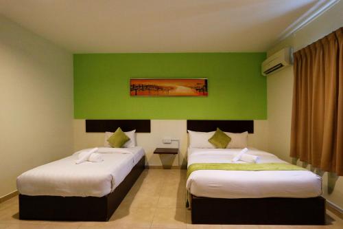 two beds in a room with a green wall at Golden Roof Hotel Falim Ipoh in Ipoh