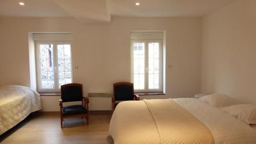 a bedroom with two beds and two chairs and two windows at Gite Notre Dame in Pontorson