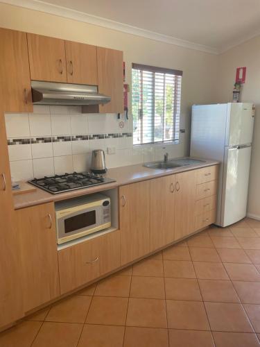 uma cozinha com armários de madeira e um frigorífico branco em Outback Oasis Caravan Park em Carnarvon