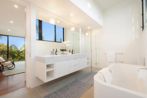 La salle de bains blanche est pourvue d'une baignoire et d'un grand miroir. dans l'établissement Byron Beachside Bliss - with pool & beach access, à Byron Bay