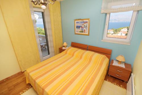 1 dormitorio con 1 cama con colcha amarilla y 2 ventanas en Family friendly house with a swimming pool Postira, Brac - 5661, en Postira