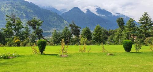 a green field with trees and mountains in the background at Anand Vardhan Resorts in Manāli