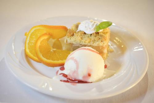 a white plate with a piece of cake with ice cream and orange slices at Hotel Mir-Jan SPA in Lądek-Zdrój
